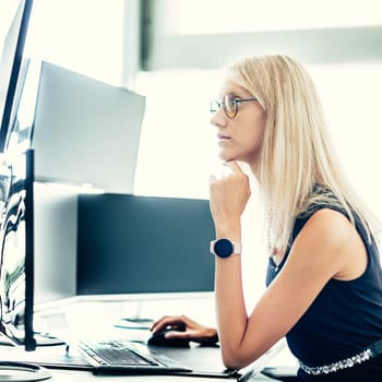 Female financial assets manager, trading online, watching charts and data analyses on multiple computer screens. Modern corporate business woman concept.