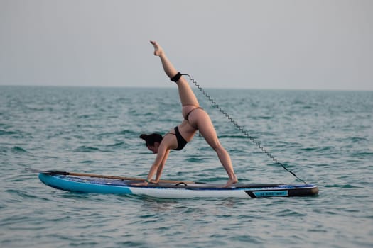 sporty girl on a sup board with a paddle in the sea does yoga