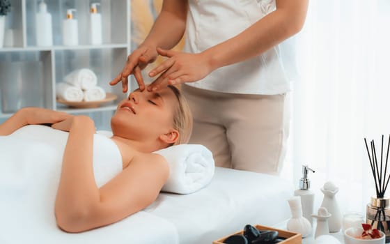 Caucasian woman enjoying relaxing anti-stress head massage and pampering facial beauty skin recreation leisure in dayspa modern light ambient at luxury resort or hotel spa salon. Quiescent