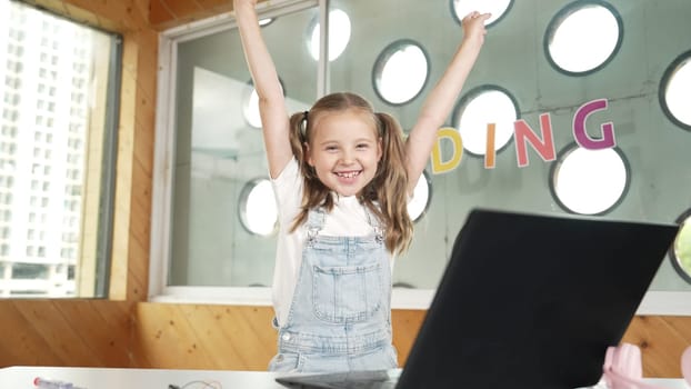 Happy girl looking at camera while raised hands to celebrate success project. Smart cute student finish writing, programing system and shouting with happiness in STEM technology class work. Erudition.