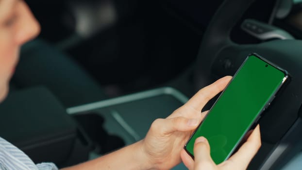 Holiday vacation road trip with environmental-friendly car concept. Eco-conscious woman on driver seat holding blank copyspace green screen smartphone for EV battery status. Exalt