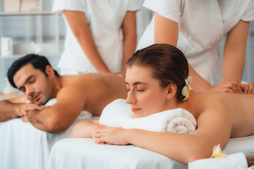 Caucasian couple customer enjoying relaxing anti-stress spa massage and pampering with beauty skin recreation leisure in day light ambient salon spa at luxury resort or hotel. Quiescent