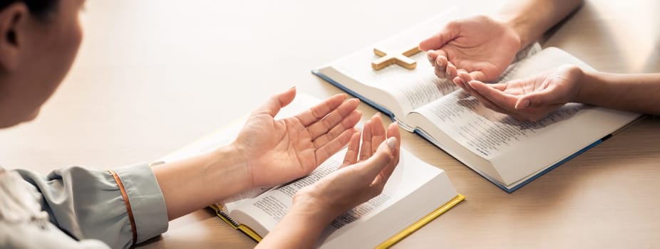 Two believer praying together on holy bible book faithfully with wooden cross placed at wooden church. Concept of hope, religion, faith, christianity and god blessing. Facing hand. Burgeoning.