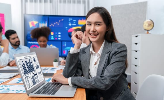 Portrait of happy young asian businesswoman with group of office worker on meeting with screen display business dashboard in background. Confident office lady at team meeting. Concord