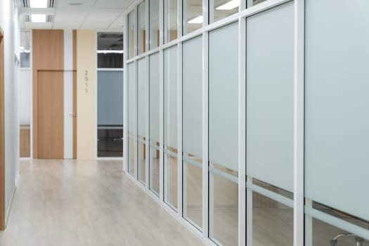 Empty modern office bright corridor with glass wall. Long white modern office hallway. No businesspeople. Many glass wall and doors. White bright empty workplace corridor background. Ornamented.