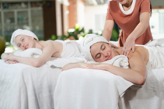A portrait of two young attractive woman lie on bed during having back massage by a professional masseur at outdoor surrounded by peaceful natural environment. Healthy and beauty concept. Tranquility.