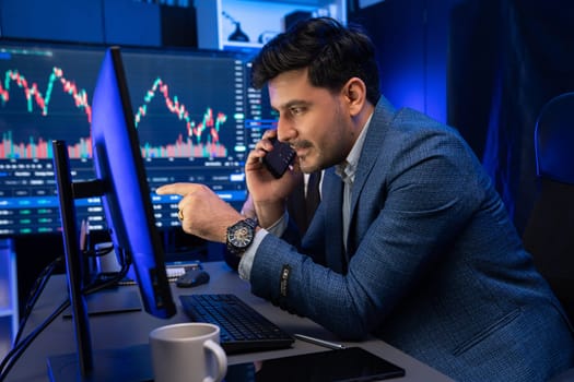 Businessman trading dynamic graph calling to broker or partner to consult high profit in exchange rate. Analyzing stock market investment growth on monitor screen in neon light at workplace. Sellable.