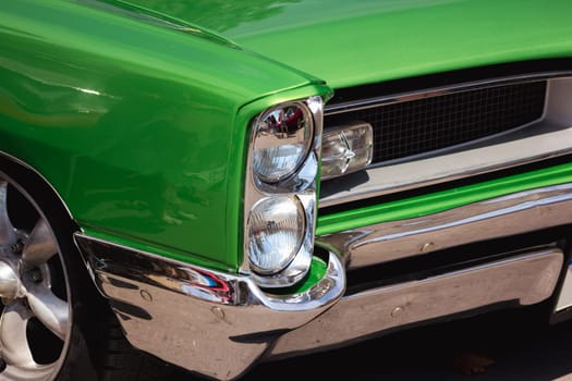 Green retro car with close-up on headlight. Front view muscle car oldtimer with chromed bumper.