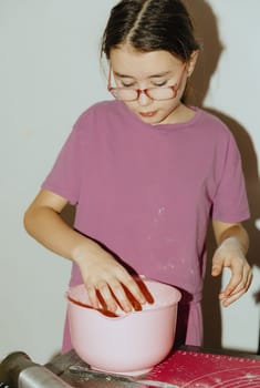 One beautiful Caucasian brunette girl stands at the table, and mixes shortbread dough with her hands in a pink bowl, close-up side view. Step by step instructions. Step 8