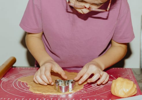 One beautiful Caucasian girl stands at the table and uses a wooden metal mold to cut out yellow shortbread dough lying on a pink silicone mat, close-up side view. Step by step instructions. Step 13