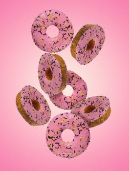 Donuts with pink glaze and sprinkled with colorful sprinkles levitate on a pink background