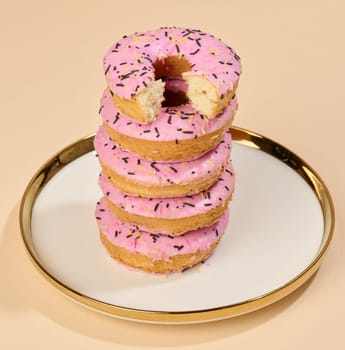Donut covered with pink glaze and sprinkled with colorful sprinkles on a round plate, brown background