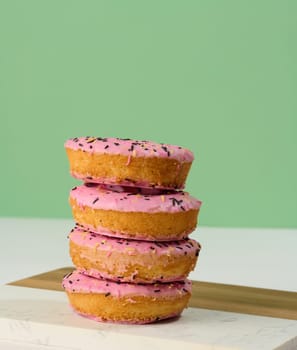 Donut covered with pink glaze and sprinkled with colorful sprinkles, green background