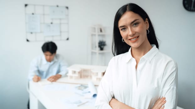 Closeup of female professional architect engineer cross arms with confident while skilled coworker focus on drawing blueprint at table with house model. Creative living and design concept. Immaculate.