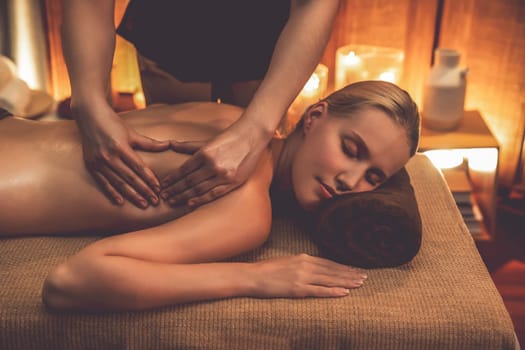 Caucasian woman customer enjoying relaxing anti-stress spa massage and pampering with beauty skin recreation leisure in warm candle lighting ambient salon spa at luxury resort or hotel. Quiescent