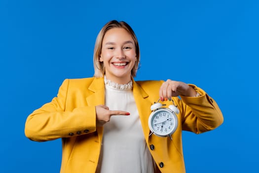 Happy student girl with alarm clock on blue background. Early morning, 6 o'clock, correct day routine, living in moment, appreciate every minute of life, youth. High quality photo