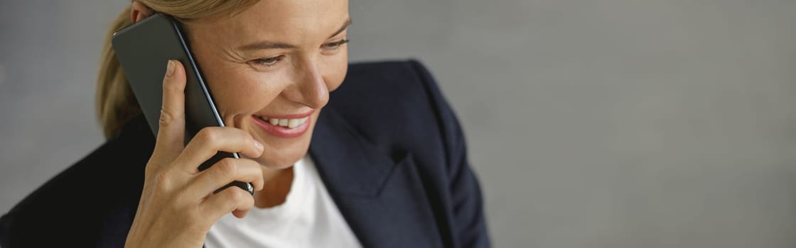 Cheerful businesswoman talking phone sitting on modern office background and looks away