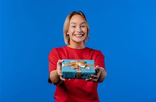 Birthday woman blonde hair with gift box on blue background. Girl smiling, she is happy with present. High quality photo