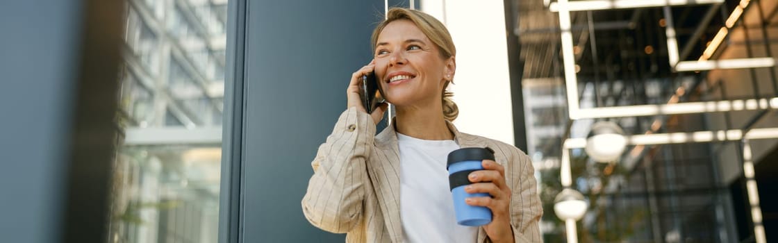 Smiling business woman talking phone while standing on building background and looks away