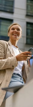 Stylish business woman use phone while sitting in modern coworking and working on laptop