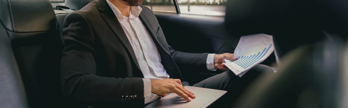 Confidence businessman sitting on car backseat and working with documents and use laptop