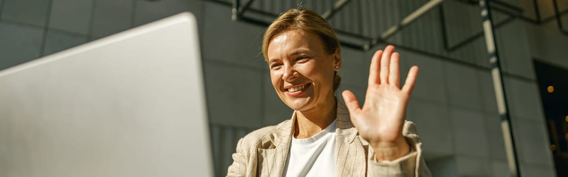 Woman freelancer talking with client via video call and waving Hi while sitting in office