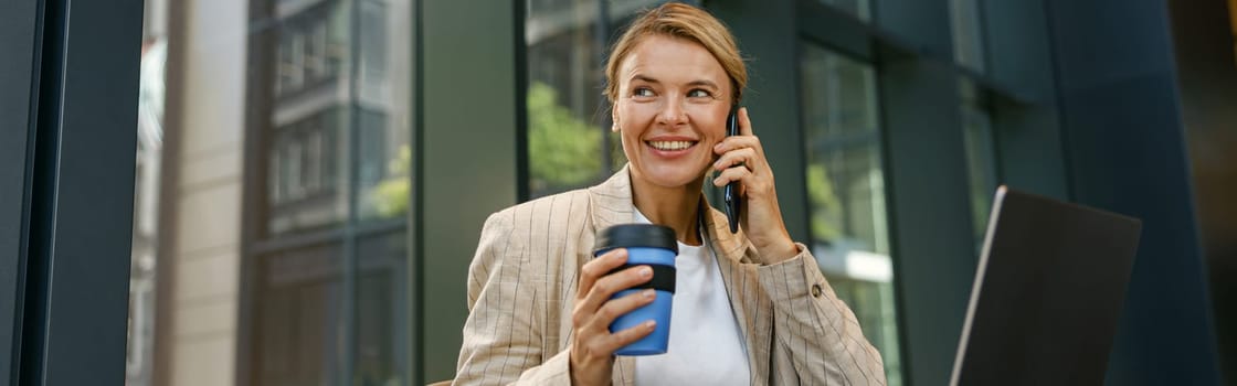 Woman freelancer talking on phone with client while working on laptop in modern coworking