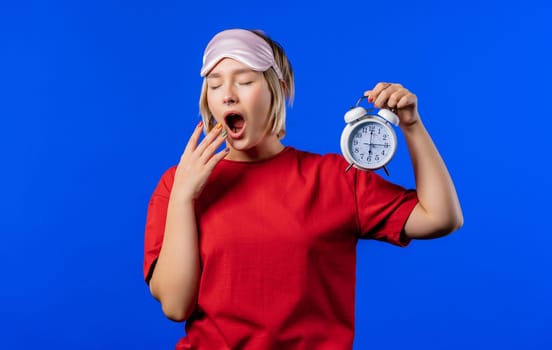 Woken up by alarm clock sleepy young woman holding it in hand. Blue background. Early 8 o'clock in morning. Lazy guy didn't get enough sleep, concept of passing time. High quality 4k
