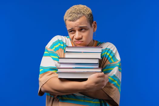 Lazy man student is dissatisfied with amount of books, homework in high school, blue background. Guy in displeasure, he is annoyed, discouraged frustrated by studies. High quality photo