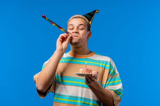 Happy birthday man making wish - blowing candle on cake. Curly haired guy laughs, celebrating anniversary. Young teenager on blue background. High quality photo