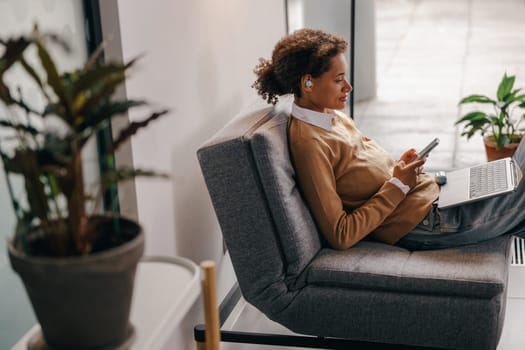 Female manager is use phone while working on laptop in modern office near window