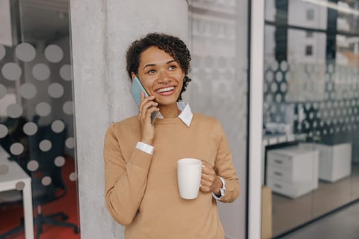 Smiling female freelancer is talking phone with client while standing on coworking background