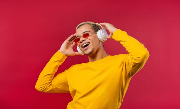 Positive man listening music, enjoying dance with headphones on red studio background. Radio, wireless modern sound technology, online player. High quality photo
