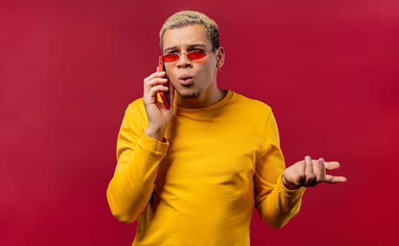 Stylish man talking by phone, nice joke, smiling. Young guy on red background. Having smartphone call. . High quality photo