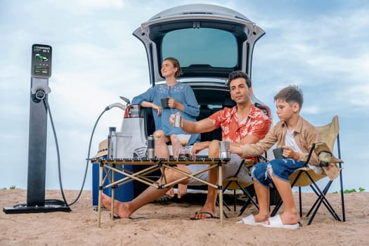 Family vacation trip traveling by the beach with electric car, happy family recharge EV car, enjoying outdoor camping coffee. Seascape travel and eco-friendly car for clean environment. Perpetual