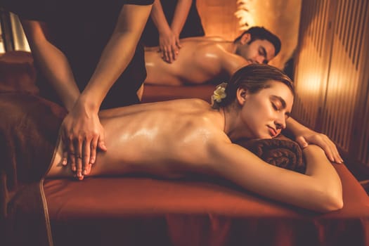 Caucasian couple customer enjoying relaxing anti-stress spa massage and pampering with beauty skin recreation leisure in warm candle lighting ambient salon spa at luxury resort or hotel. Quiescent