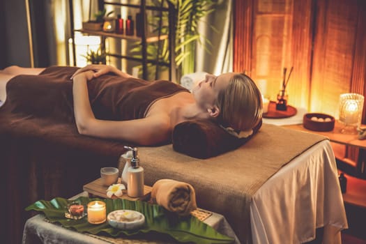 Caucasian woman customer enjoying relaxing anti-stress spa massage and pampering with beauty skin recreation leisure in warm candle lighting ambient salon spa at luxury resort or hotel. Quiescent