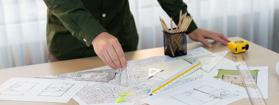 A portrait of architect using divider to measure blueprint. Architect designing house construction on a table at studio, with architectural equipment scattered around. Focus on hand. Delineation