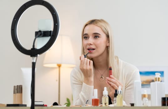 Young woman making beauty and cosmetic tutorial video content for social media. Beauty blogger using camera and light ring while showing how to apply liquid lipstick to audience or follower. Blithe