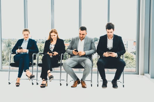 Businesswomen and businessmen using mobile phone while waiting on chairs in office for job interview. Corporate business and human resources concept. uds