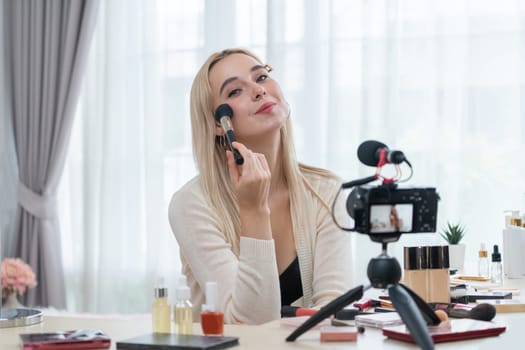 Young woman making beauty and cosmetic tutorial video content for social media. Beauty blogger smiles to camera while showing how to apply mascara to audience or followers. Blithe