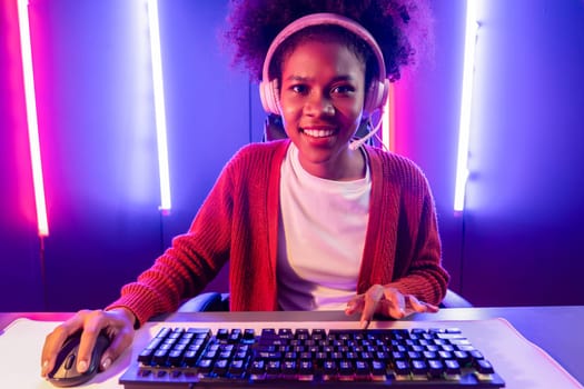 Gaming streamer, African girl playing online fighting with Esport skilled team wearing headphones in neon color lighting room. Talking other players planing strategies to win competitors. Tastemaker.