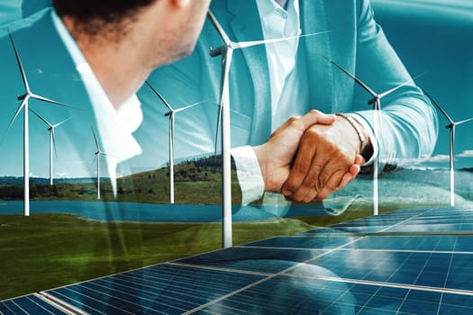 Double exposure graphic of business people handshake over wind turbine farm and green renewable energy worker interface. Concept of sustainability development by alternative energy. uds