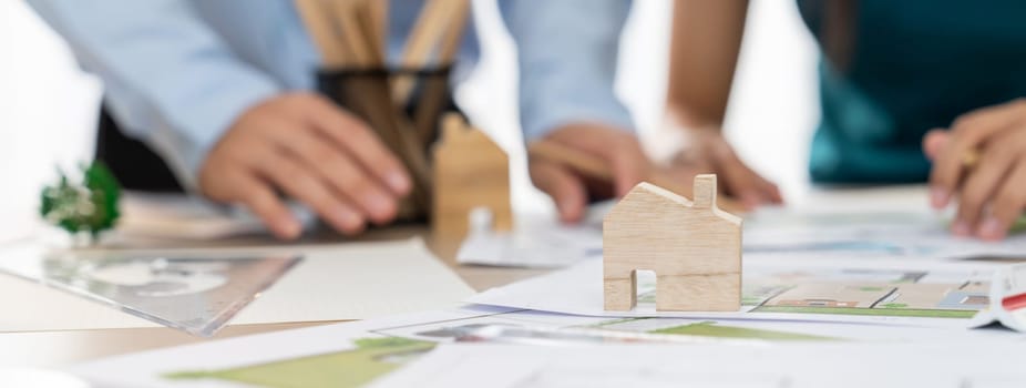 A portrait of professional architect team discussion about architectural project on meeting table with blueprint and wooden block scatter around at modern office. Closeup. Focus hand. Delineation.