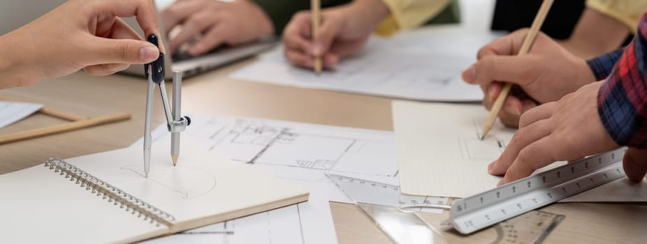 Skilled architect team using architectural equipment during colleague discussion about building design at meeting table with blueprint scatter around. Closeup. Focus on hand. Delineation.