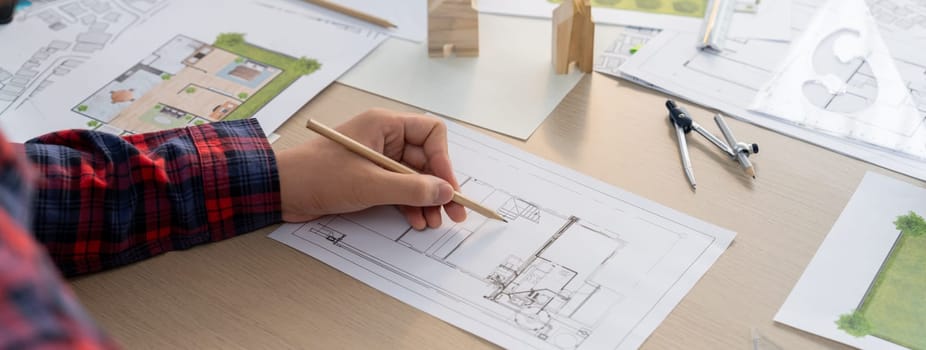 Closeup of architect engineer hand using ruler to mature and draw a blueprint on meeting table with wooden block, pencil and blueprint scatter around at architectural modern office. Delineation.