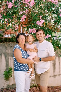 Little girl sits in the arms of her grandmother standing next to her father under a flowering tree in the garden. High quality photo