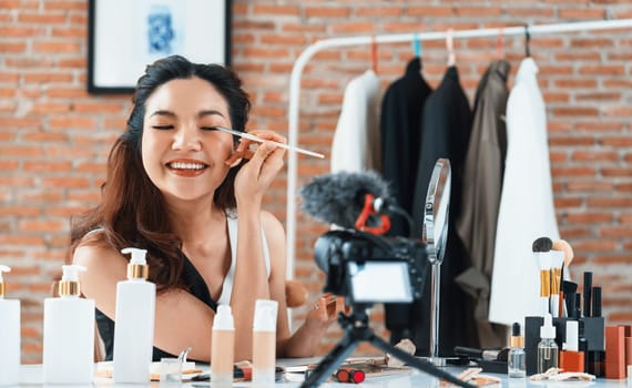 Asian Woman influencer shoot live streaming vlog video review makeup uttermost social media or blog. Happy young girl with cosmetics studio lighting for marketing recording session broadcasting online