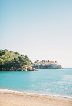 View from the sandy beach of the island of Sveti Stefan, looking out from behind a wooded cliff. Montenegro. High quality photo