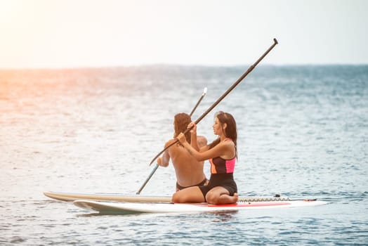 Sea woman and man on sup. Silhouette of happy young woman and man, surfing on SUP board, confident paddling through water surface. Idyllic sunset. Active lifestyle at sea or river